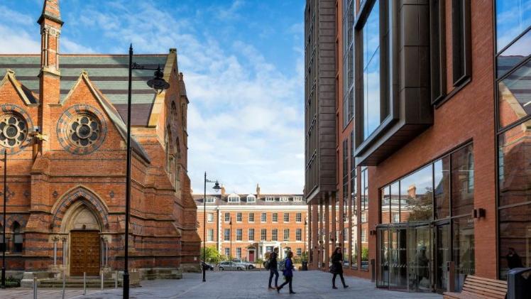 old red brick building on left and modern glass and red brick building on right, with paved plaza in between